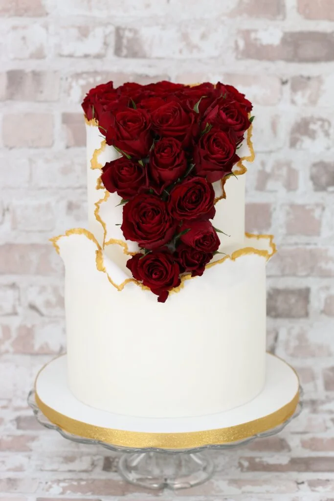 white 2-tier wedding cake with painted gold edges and fresh deep red roses